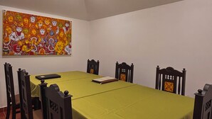 A dining room with a green table, wooden chairs, a ceiling fan, and a colorful painting on the wall. - SURYAMANGALAM HERITAGE (Ottapalam)