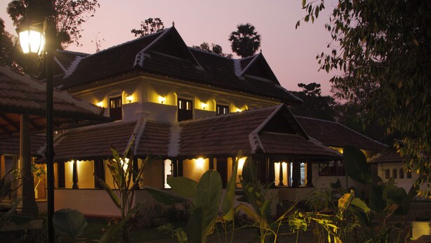 A large, multi-story building with a traditional architectural style, featuring a tiled roof and multiple illuminated windows. - SURYAMANGALAM HERITAGE (Ottapalam)