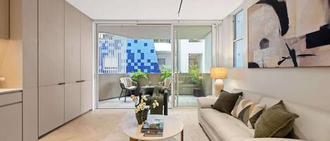 A modern living room with a sofa, coffee table, and a view of a blue-tiled building through a glass door.