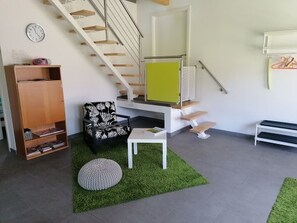 A modern living room with a staircase, a sofa, a small table, and a bookshelf. - Appartement - Les Poingnats, (Les Breuleux), by Interhome (Les Breuleux)