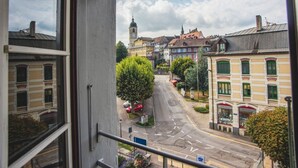 Blick aus einem Fenster auf eine Straße mit Gebäuden, einem Baum und blauem Himmel.