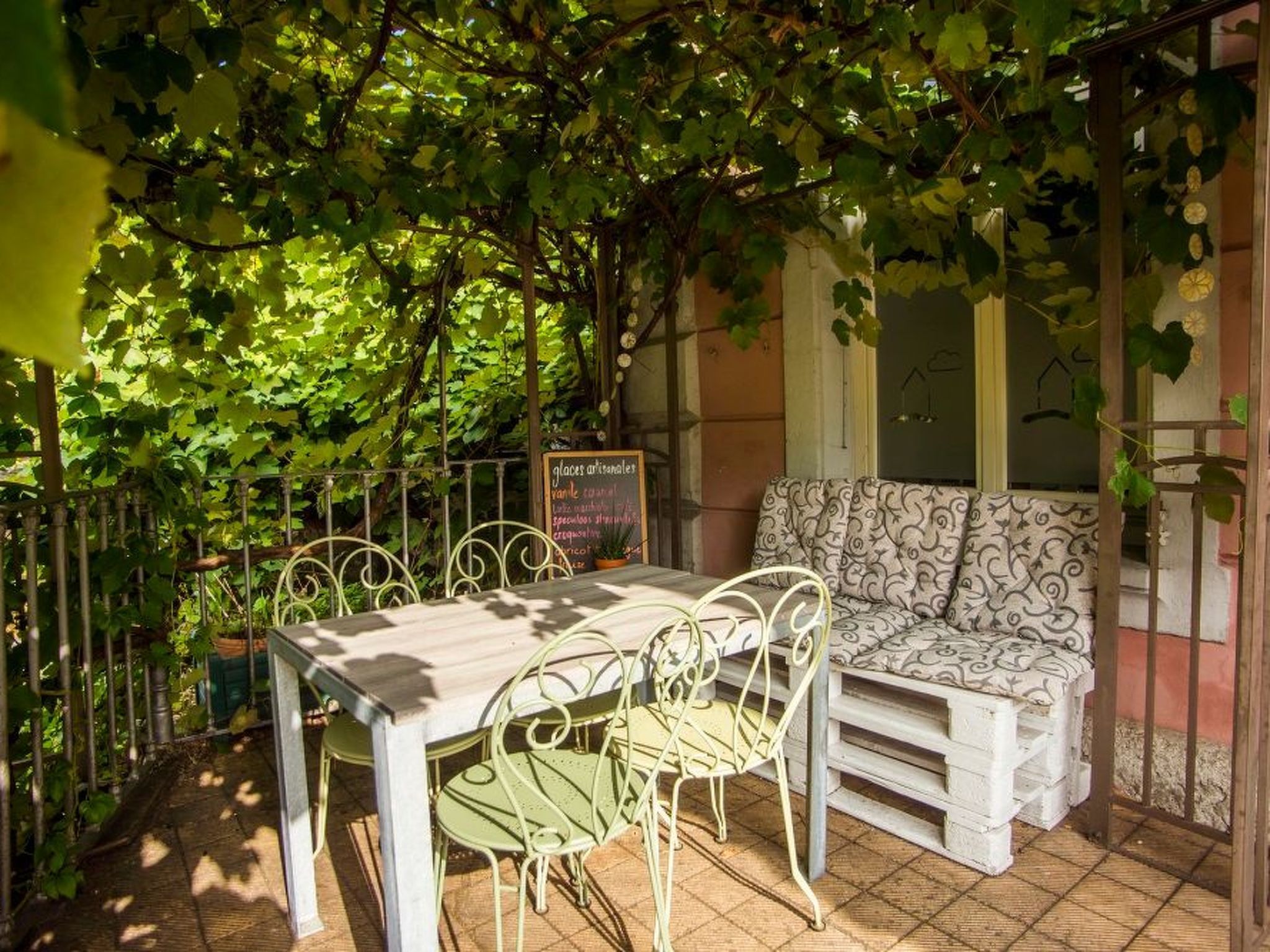An outdoor seating area with a table and chairs, surrounded by greenery and a tiled floor.