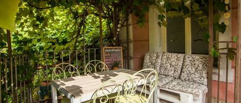 An outdoor seating area with a table and chairs, surrounded by greenery and a tiled floor.