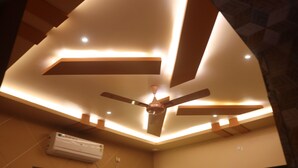 A ceiling fan with recessed lighting, a wall-mounted air conditioner, and a geometric ceiling design. - Vrindavan Guest house  (Ambegaon)