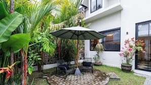 A circular patio with a brick pattern, surrounded by lush greenery and two wicker chairs with cushions. - Orfeas Villas 2 Canggu Villa 2BR Pool (Canggu)