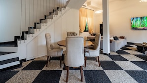 A modern interior with a staircase, a dining area with chairs and a table, a sofa, and a large TV on the wall. - Orfeas Villas 2 Canggu Villa 2BR Pool (Canggu)