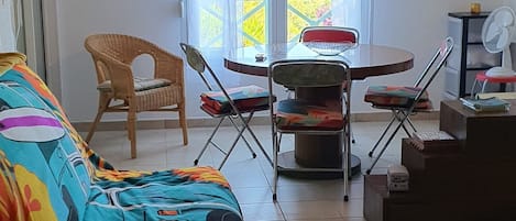 Ein Zimmer mit einem farbenfrohen Sofa, einem Esstisch mit Stühlen, einem Deckenventilator und Blick durch ein großes Fenster.