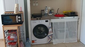 Une cuisine compacte équipée d’un lave-linge, d’un four à micro-ondes et d’un petit évier.