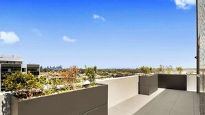 Une terrasse sur le toit offrant une vue sur les toits d’une ville, un bâtiment moderne et quelques espaces verts.