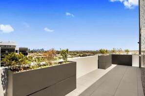 A rooftop terrace with a view of a city skyline, a modern building, and some greenery. - Spacious New 2 BDR with City Views (Northcote)