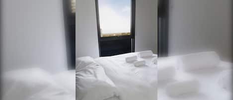 A hotel room with a bed, pillows, and a view through a window.