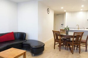 A living room with a black leather sofa, a wooden coffee table, and a dining area with wooden chairs and a table.