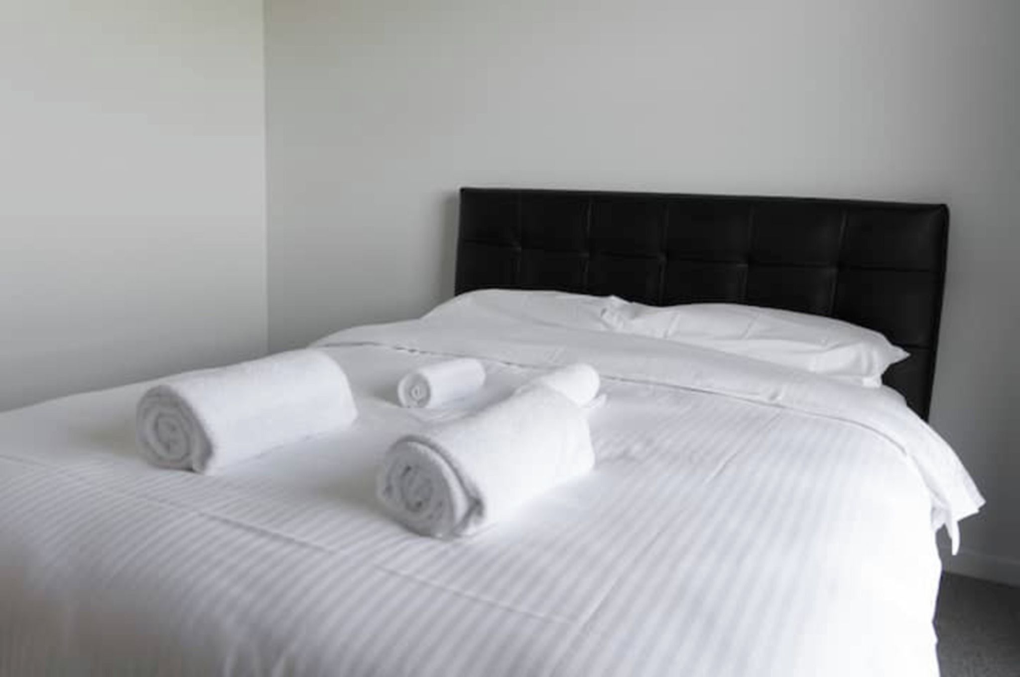 Een net opgemaakt bed met witte lakens en opgerolde handdoeken.