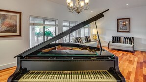A grand piano in a spacious room with hardwood flooring, large windows, a chandelier, and a sofa. - Resort-Style Home with Backyard & Heated Pool : A Luxe Tucson Home (Tucson)