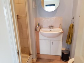 Un baño con un lavamanos blanco, un espejo encima, una toalla colgada en un perchero y un inodoro.