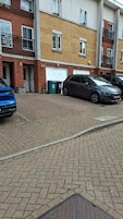 Un edificio residencial de varios pisos con fachadas de ladrillo y color crema, un camino pavimentado y coches estacionados.