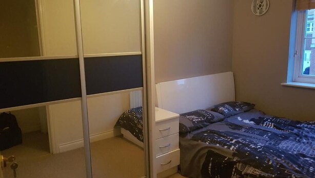A bedroom with a bed, a wardrobe, a mirror, and a window.