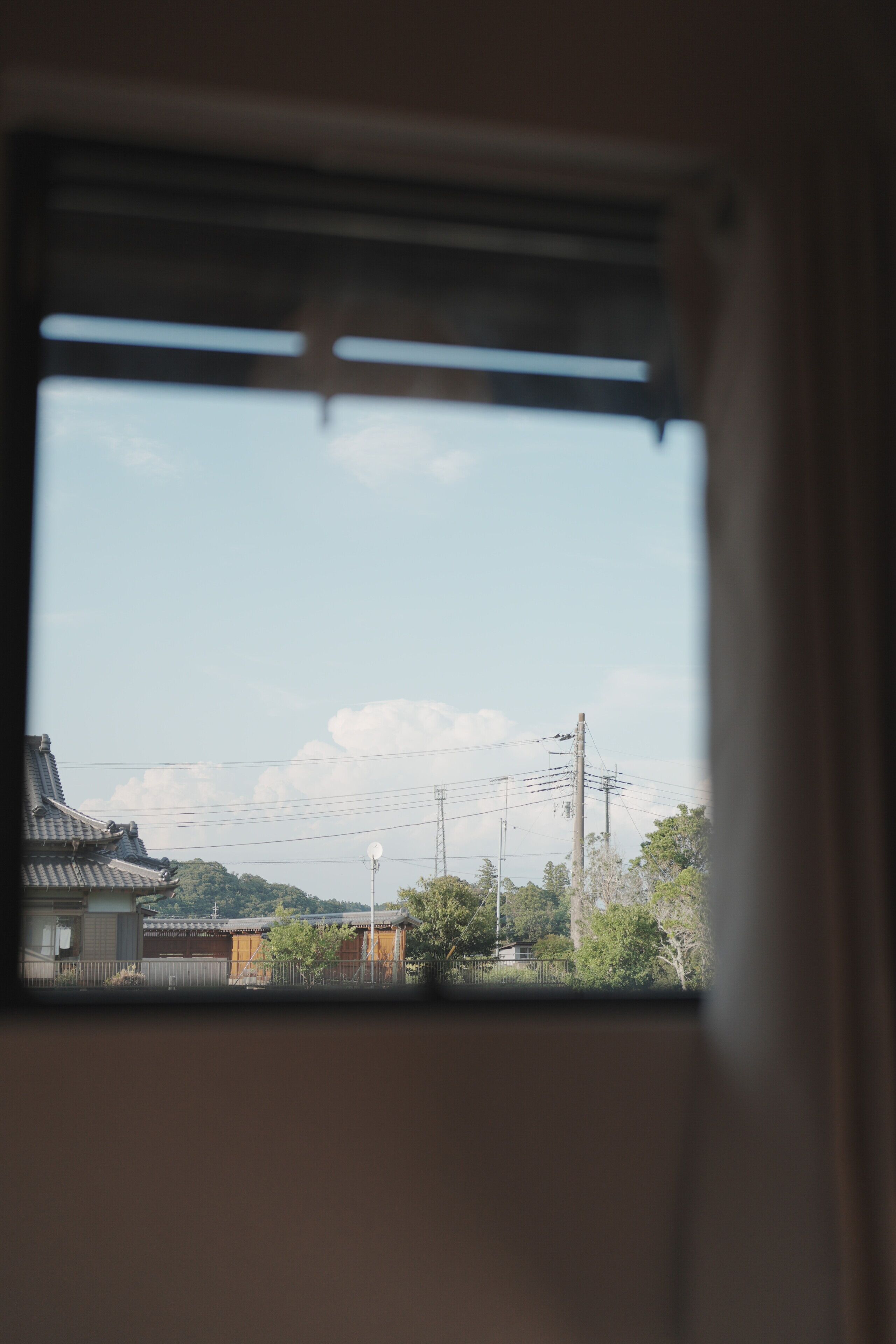 A window view of a traditional building with a tiled roof, surrounded by greenery and utility poles.