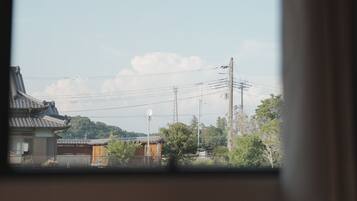 A window view of a traditional building with a tiled roof, surrounded by greenery and utility poles.