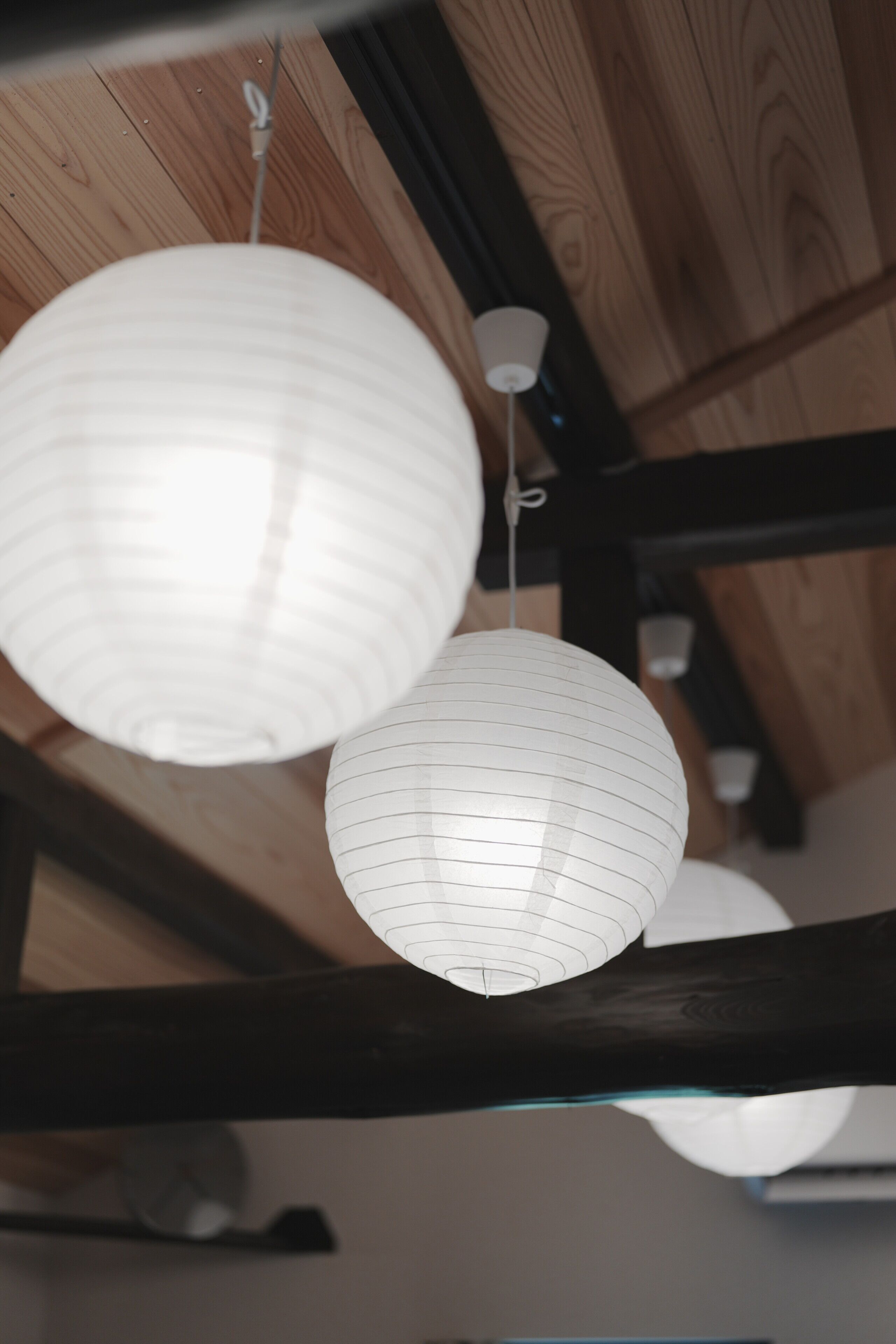 Two white paper lanterns hanging from a wooden ceiling.