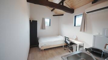A small, clean room with a bed, desk, and kitchenette.
