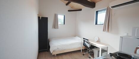 A small, clean room with a bed, desk, and kitchenette.