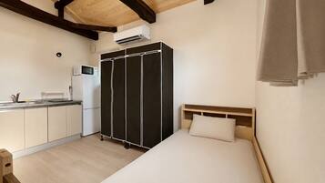A compact room with a kitchenette, a bed, and a wardrobe.