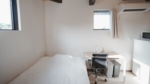 A bedroom with a bed, a desk, a chair, an air conditioner, a window, and a view of the city.