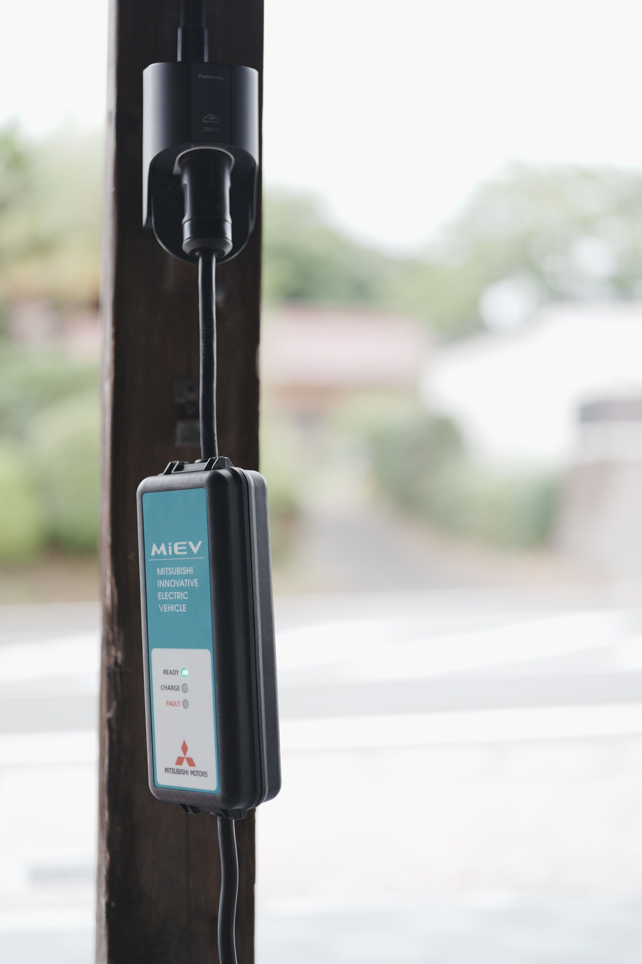 A Mitsubishi electric vehicle charging station attached to a wooden post.