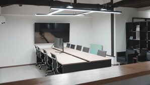 A conference room with a long table, chairs, a large flat-screen TV, and modern lighting.