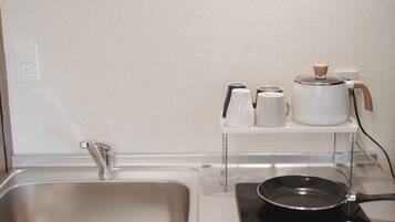 A kitchen with a stainless steel sink, a kettle, a coffee maker, and a frying pan on a portable stove.