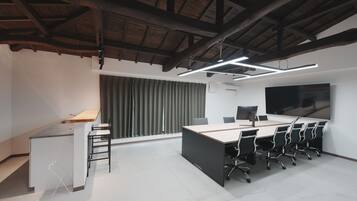 A modern office space with a large desk, multiple chairs, a large screen, and a window with curtains.