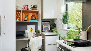Cocina compacta con estufa, un refrigerador pequeño, una zona de comedor con una silla y una ventana con plantas.