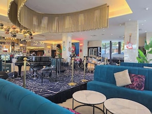Eine Lobby mit einem Flügel, einer Bühne mit Musikinstrumenten, einer Bar und Sitzgelegenheiten.
