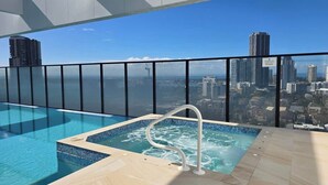 En pool på taket med utsikt över staden, ett bubbelbad och ett glasräcke.