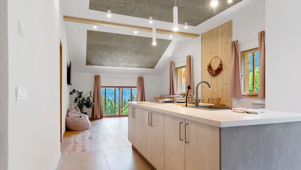 A modern kitchen with a large island, wooden cabinets, and a view of greenery outside.