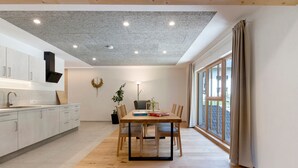 Una cocina moderna con gabinetes blancos, una mesa de comedor con sillas, un techo con luces empotradas y un ventanal con cortinas.