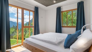 Une chambre à coucher avec un lit en bois, de grandes fenêtres et une vue sur la verdure.
