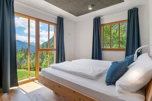 Un dormitorio con cama de madera, ventanas amplias y vista a zonas verdes.