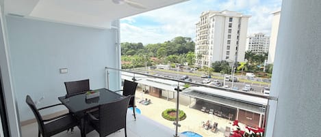 A balcony with a table and chairs, a ceiling fan, and a view of a parking lot and buildings.