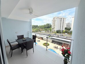Ein Balkon mit Tisch und Stühlen, einem Deckenventilator und Blick auf einen Parkplatz sowie Gebäude.