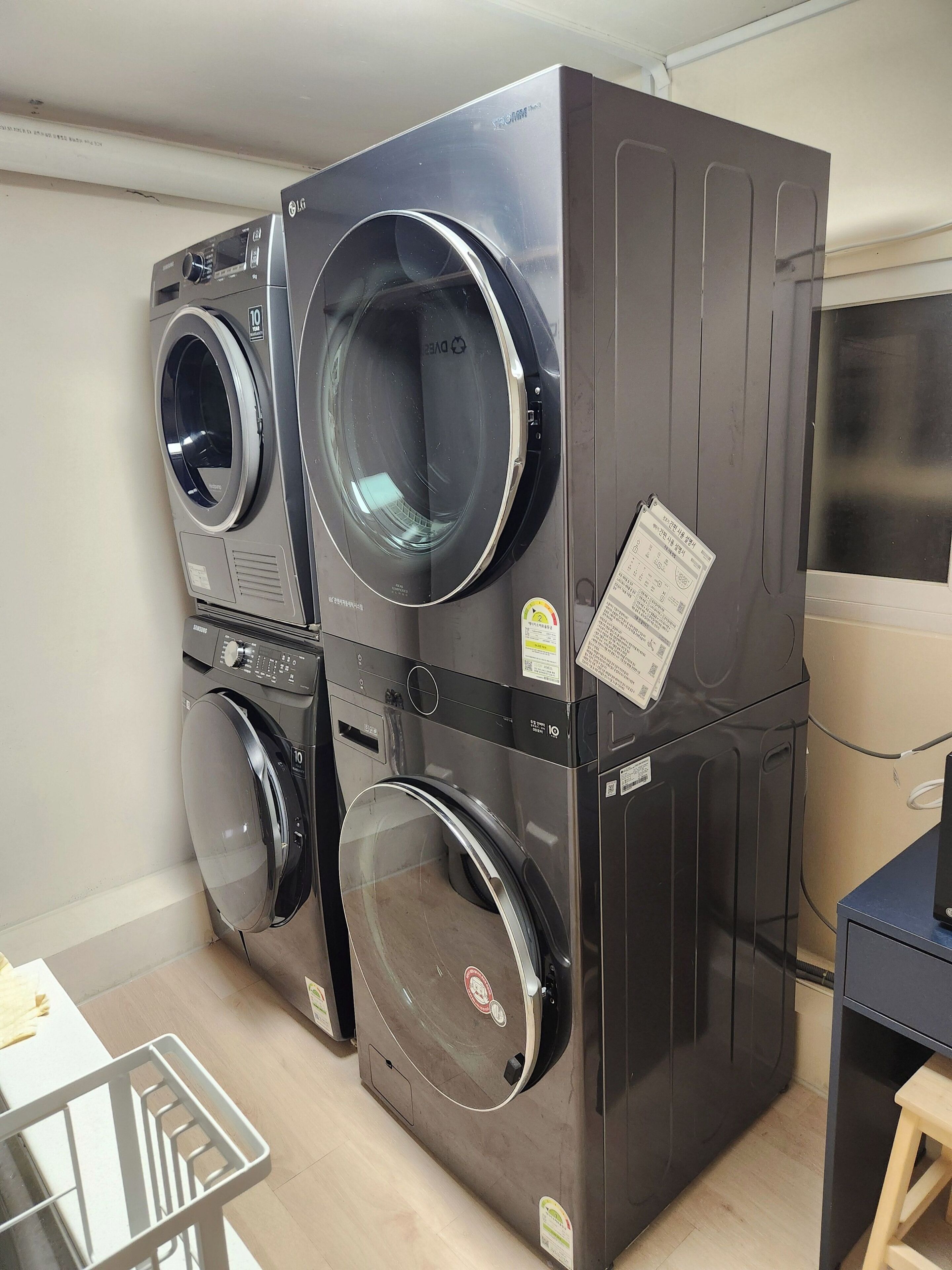 Een gestapelde wasmachine en droger in een kamer met een houten vloer en een kleine tafel.