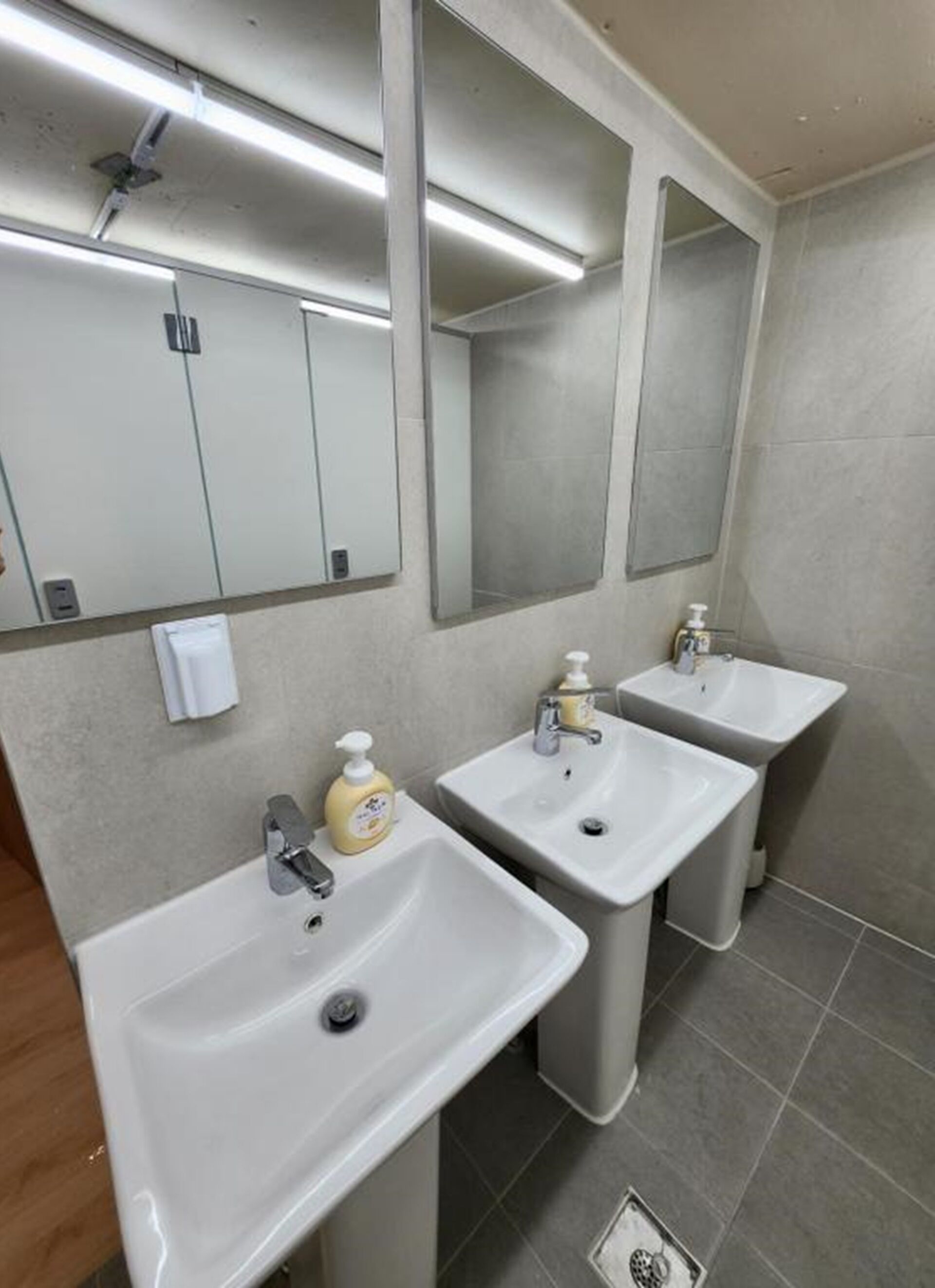 Un baño con tres lavamanos, un espejo y dispensador de jabón.