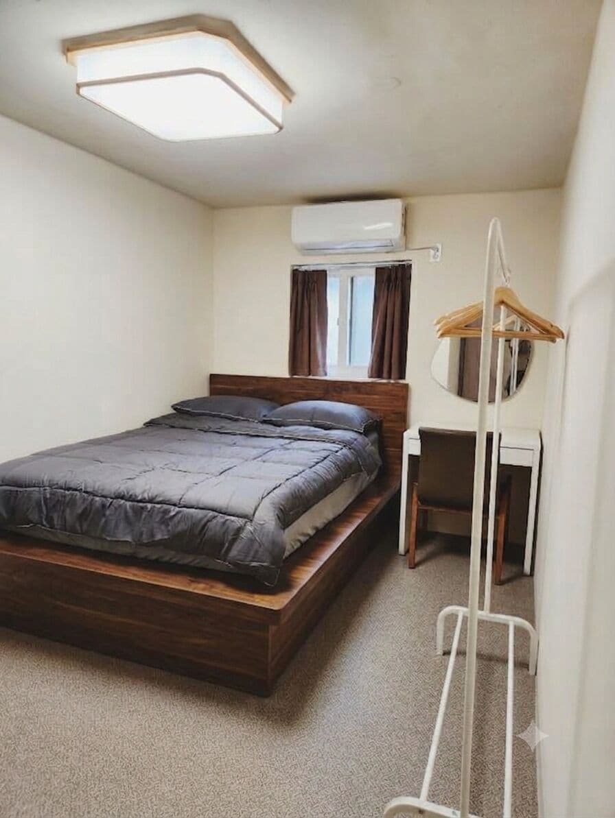 Een kleine slaapkamer met een bed, bureau en kledingrek.