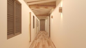 Un pasillo con vigas de madera, suelo de baldosas y una lámpara fijada a la pared.