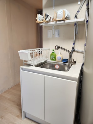 A compact kitchen with a sink, a dish rack, and a small shelf with dishes and a bottle. - Zen Seoul Stay (Seoul)