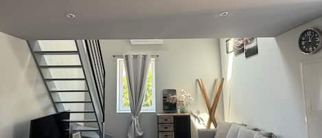 A modern living room with a flat-screen TV, a sofa, a staircase, and a window with curtains.