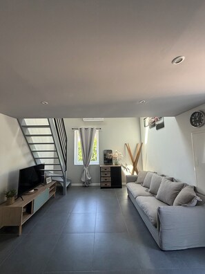 Ein modernes Wohnzimmer mit Flachbildfernseher, einer Couch, einer Treppe und einem Fenster mit Vorhängen.