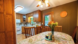 Une cuisine avec des meubles en bois, un four à micro-ondes et une table à manger recouverte d’une nappe à motifs floraux.