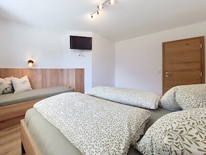 A modern bedroom with a bed, a sofa, a TV mounted on the wall, and a wooden door.